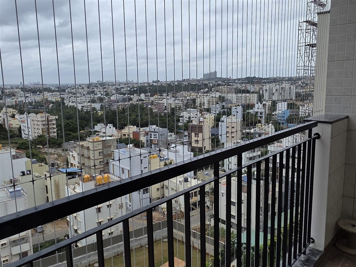 Invisible grill wires on a high-rise balcony overlooking a residential complex's sports court and grounds