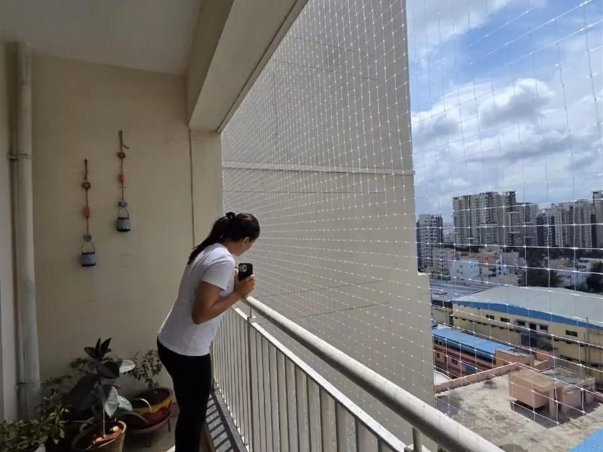 Resident standing on a balcony fitted with a pigeon net, overlooking the city